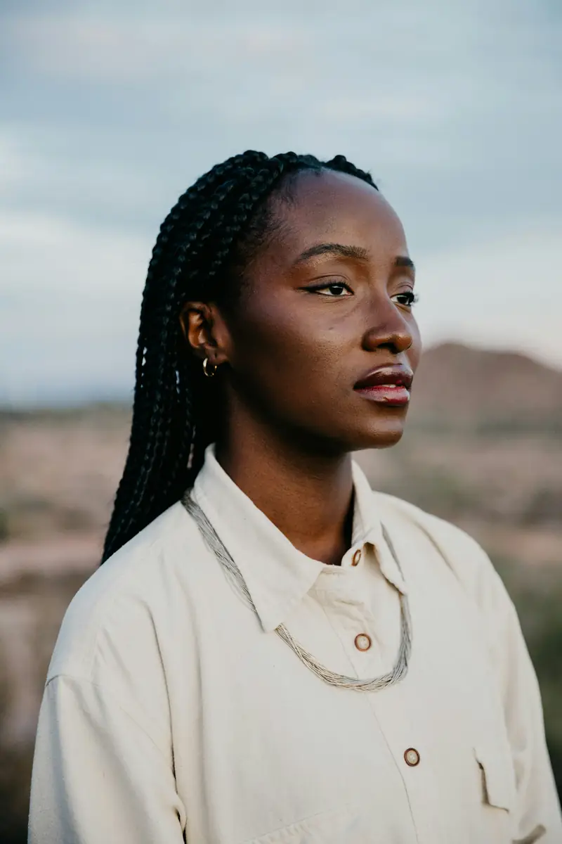 Woman with long braids in a cream jacket by the sea